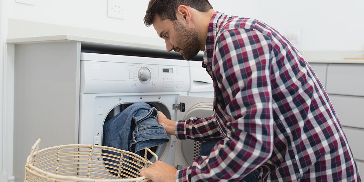 Side view of Caucasian man putting dirty clothes into the washing machine in a comfortable home